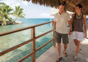 Couple walking along overwater bungalow boardwalk in Huahine French Polynesia during South Pacific cruise