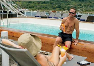 Couple relaxing poolside with tropical cocktails aboard luxury South Pacific cruise in the Cook Islands and Society Islands